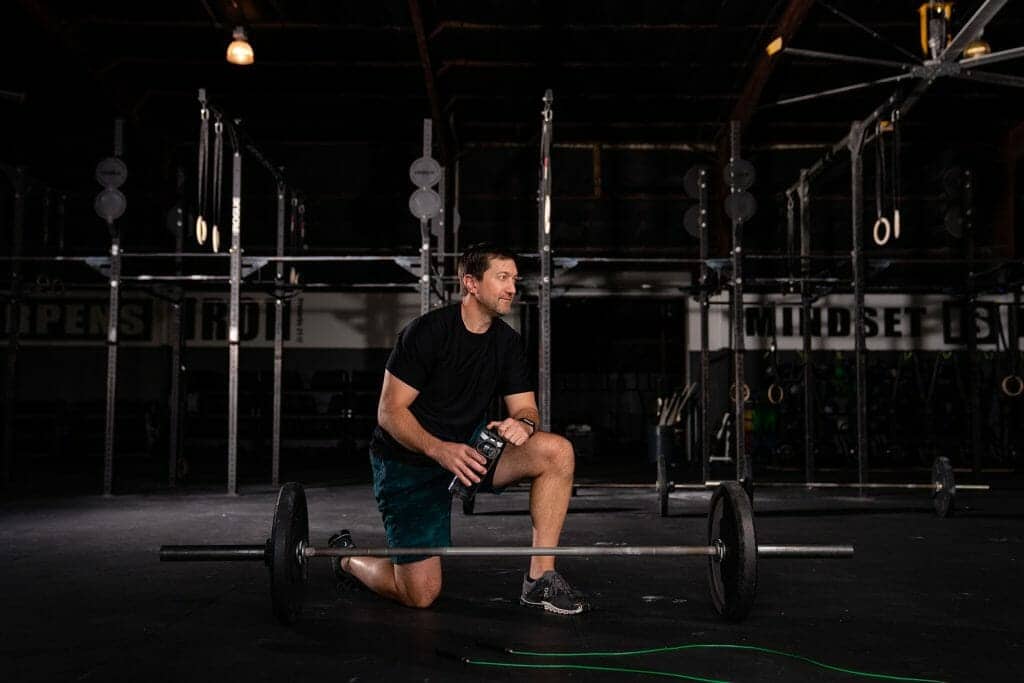 A man performing squats with a barbell under the supervision of an orthopedist in a gym.