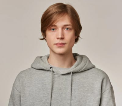 A person with straight hair wearing a gray hoodie stands against a neutral background.