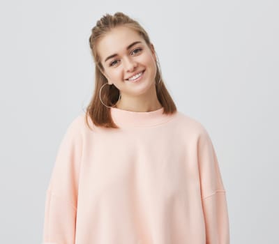 A person wearing a light pink sweatshirt smiles at the camera against a plain background.